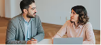 Homem e mulher sentados em uma mesa em uma conversa séria com um notebook à frente.