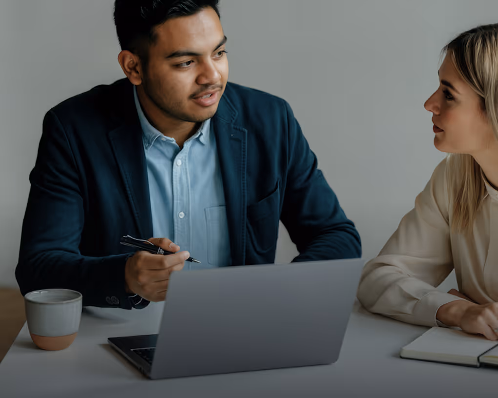 Dois colegas discutindo trabalho em um notebook em um ambiente de escritório moderno.