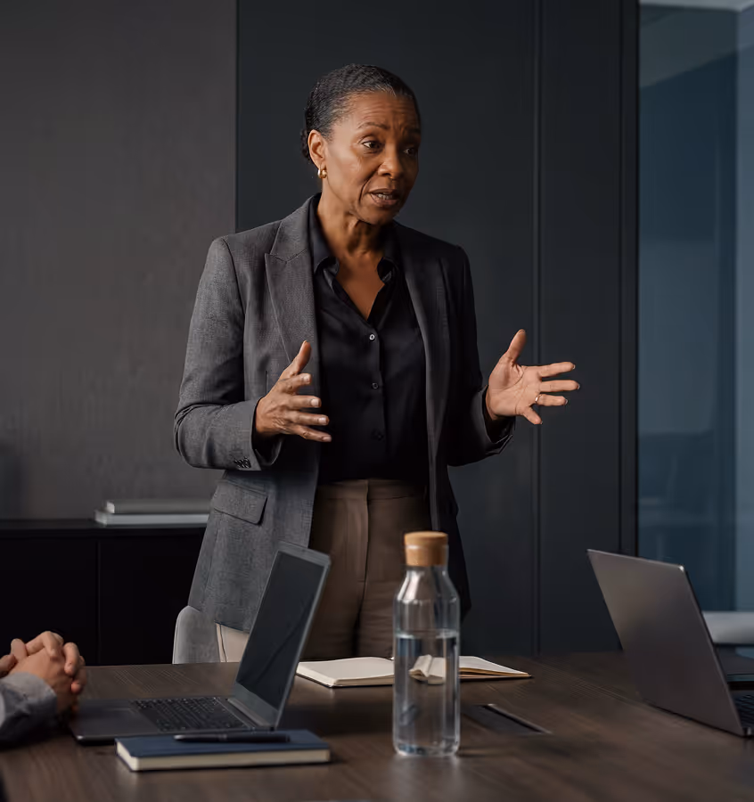 Empresária falando e gesticulando com as mãos durante uma reunião em um escritório moderno.