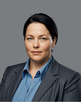 Mulher profissional de cabelo escuro usando camisa azul e blazer listrado contra um fundo cinza.