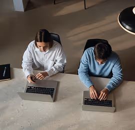 Duas pessoas digitando em notebooks em uma mesa, vistas de cima.