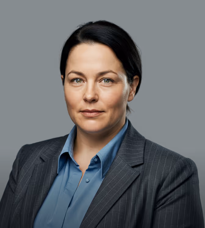 Mulher profissional de cabelo escuro usando camisa azul e blazer listrado contra um fundo escuro.