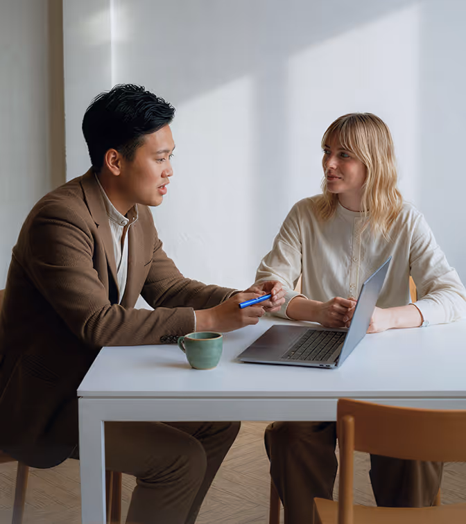 Dois profissionais conversando em uma mesa com um notebook e uma x&iacute;cara de caf&eacute;.